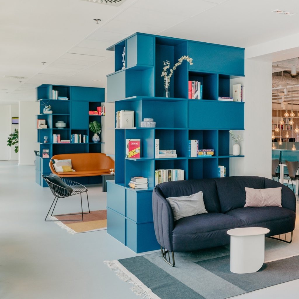 1st floor in Hotel Casa with with a brown sofa and a blue dark grey sofa, behind them are two blue shelves with some books. This place can used to enjoy coffee and do remote work